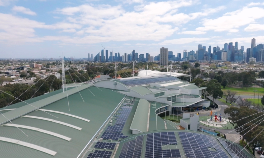 Aerial view of a green-roofed building with solar panels, with a distant city skyline of tall buildings. Aerial view of a green-roofed building with solar panels, with a distant city skyline of tall buildings.