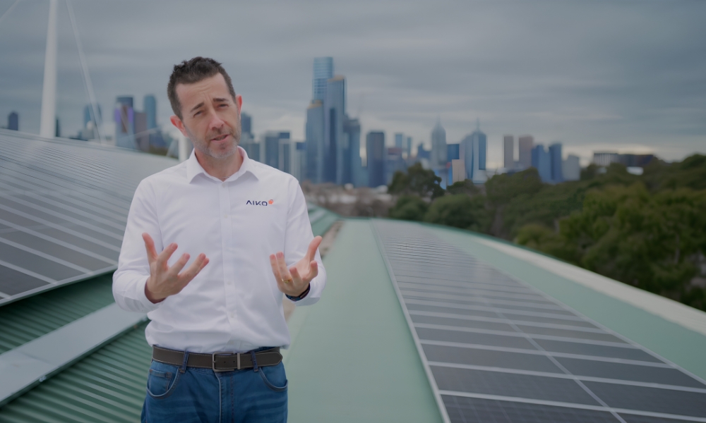 Man in a white shirt with a logo standing on a rooftop covered with solar panels, city skyline in the background at dusk/daylight. Man in a white shirt with a logo standing on a rooftop covered with solar panels, city skyline in the background at dusk/daylight.