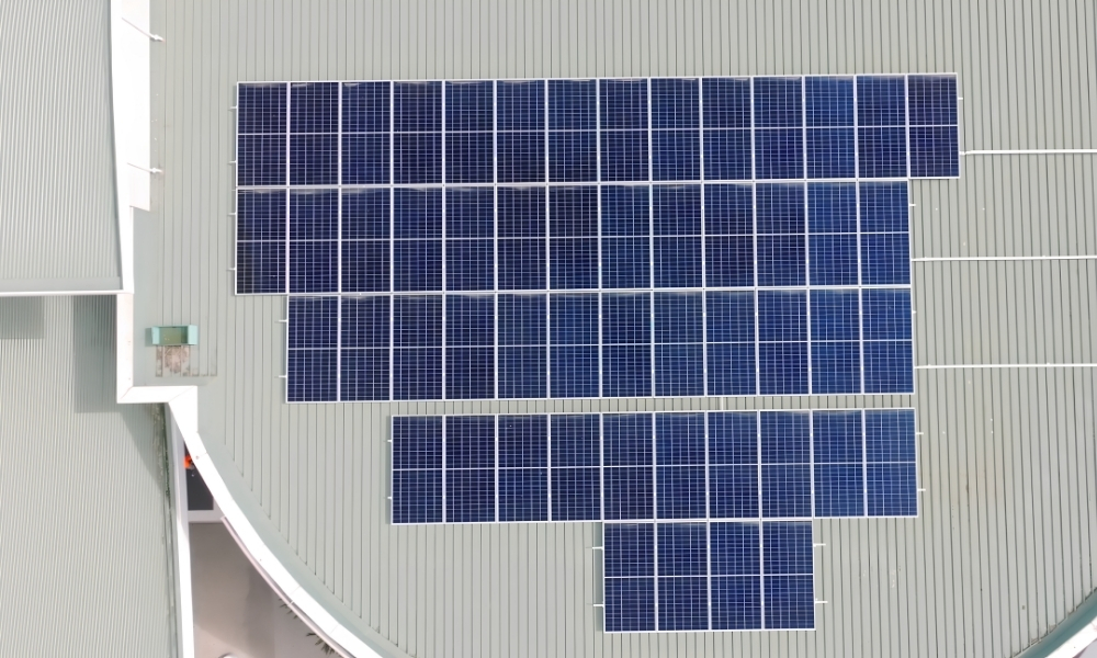 Top-down view of a building roof covered with blue solar panels arranged in a grid Top-down view of a building roof covered with blue solar panels arranged in a grid