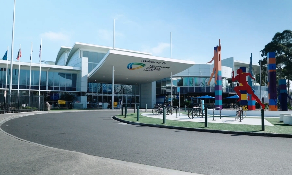 Exterior of a modern convention center with a curved canopy entrance, flagpoles, and bike racks in a plaza with colorful sculptures nearby. Exterior of a modern convention center with a curved canopy entrance, flagpoles, and bike racks in a plaza with colorful sculptures nearby.