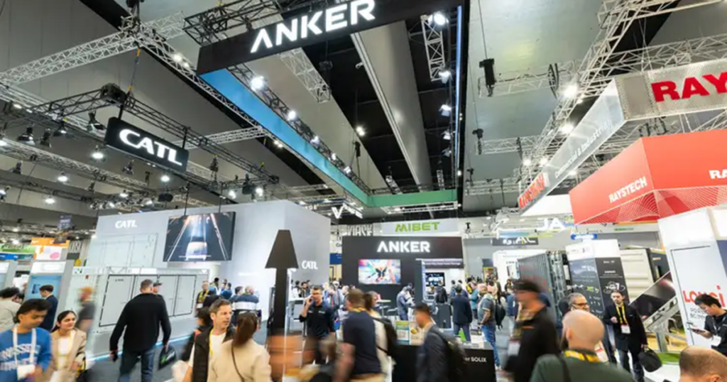 Crowded tech trade show floor with large booths and hanging brand signs like ANKER and CATL above the crowd. Crowded tech trade show floor with large booths and hanging brand signs like ANKER and CATL above the crowd.