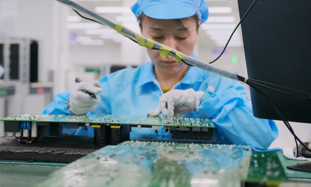 Worker in blue protective suit soldering an electronic circuit board in a manufacturing setting Worker in blue protective suit soldering an electronic circuit board in a manufacturing setting