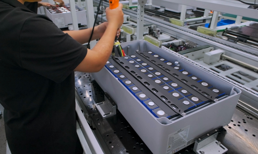 Technician using a handheld tool to wire or assemble cylindrical batteries in a tray on a factory line. Technician using a handheld tool to wire or assemble cylindrical batteries in a tray on a factory line.