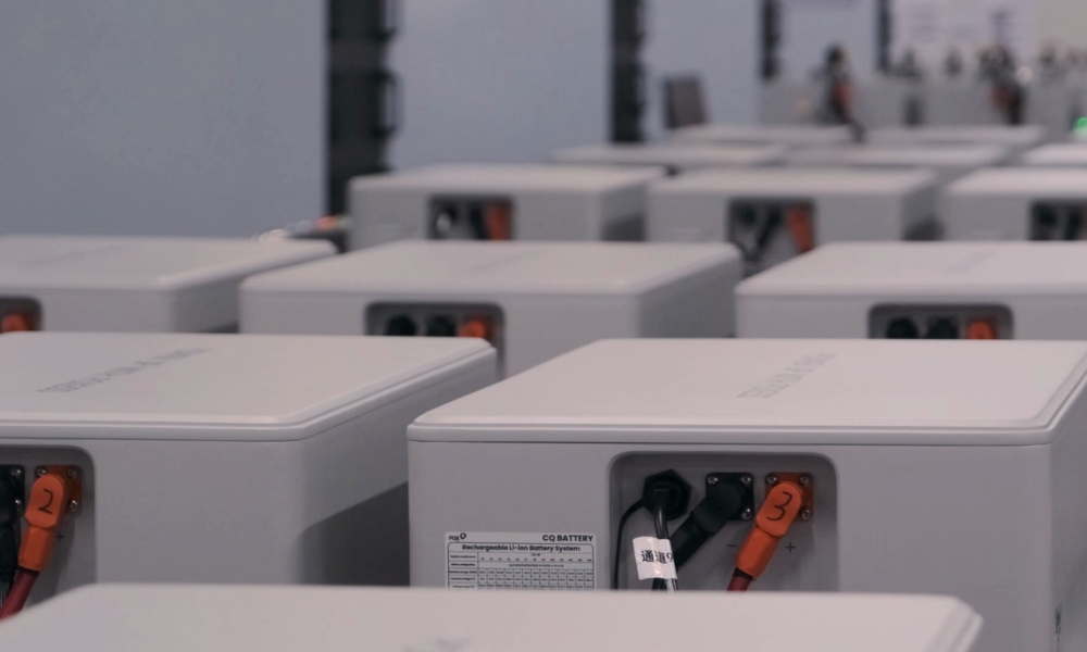 Rows of gray industrial battery modules with orange terminals and black cables in a warehouse-like setting, front units in focus Rows of gray industrial battery modules with orange terminals and black cables in a warehouse-like setting, front units in focus