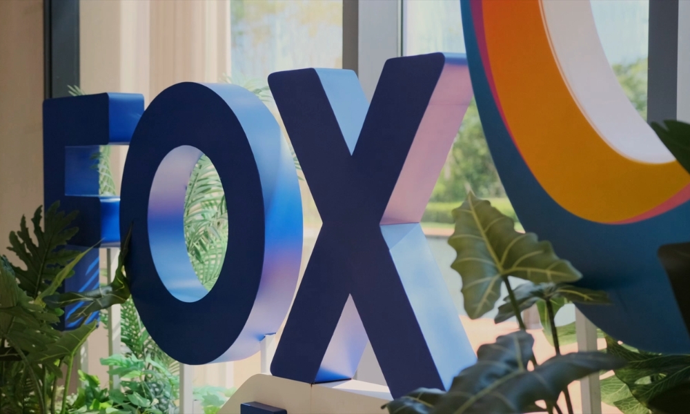 Oversized glossy blue letters spell 'FOX' in a sunlit lobby with green plants around. Oversized glossy blue letters spell 'FOX' in a sunlit lobby with green plants around.