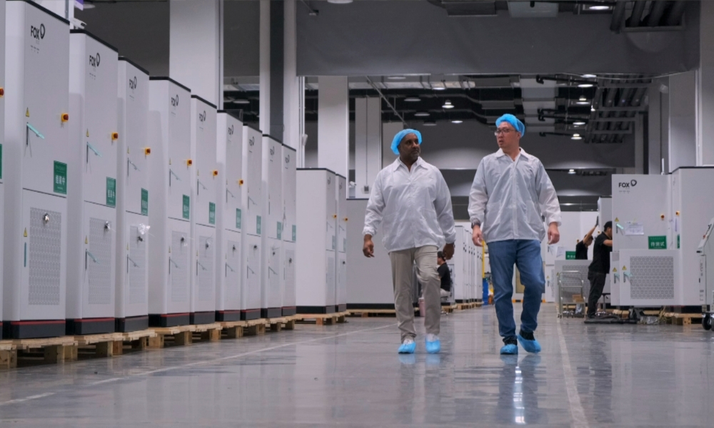 Two workers in white lab coats and blue hair nets walk down a clean factory aisle between rows of tall white industrial cabinets on pallets by the walls. Two workers in white lab coats and blue hair nets walk down a clean factory aisle between rows of tall white industrial cabinets on pallets by the walls.