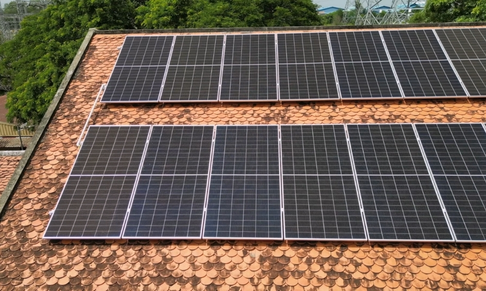 Row of solar panels mounted on a red clay tile roof with greenery in the background. Row of solar panels mounted on a red clay tile roof with greenery in the background.