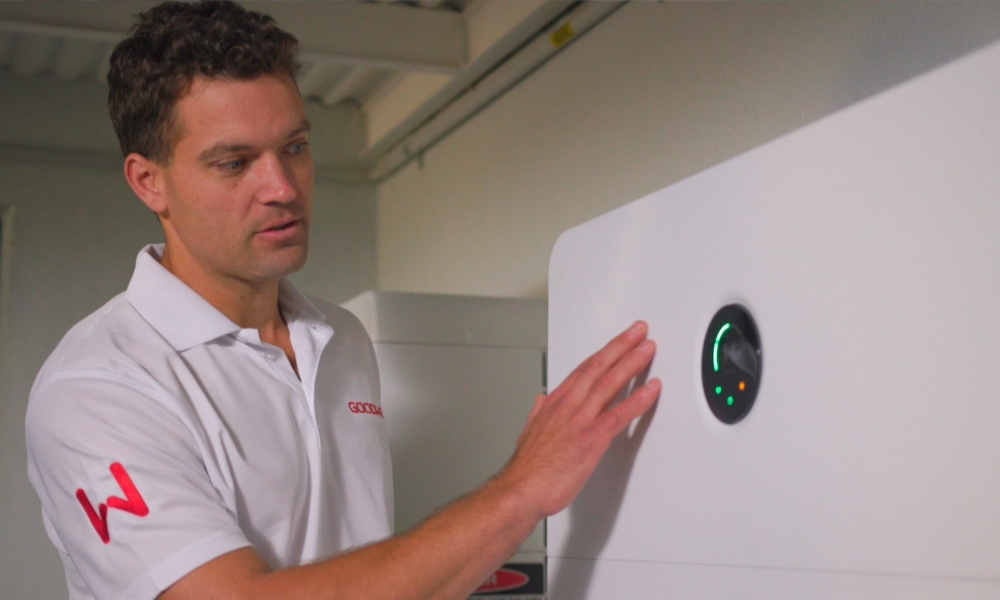 Man in a white polo shirt touches a large white industrial machine with a circular control panel displaying a green arc and orange indicators. Man in a white polo shirt touches a large white industrial machine with a circular control panel displaying a green arc and orange indicators.
