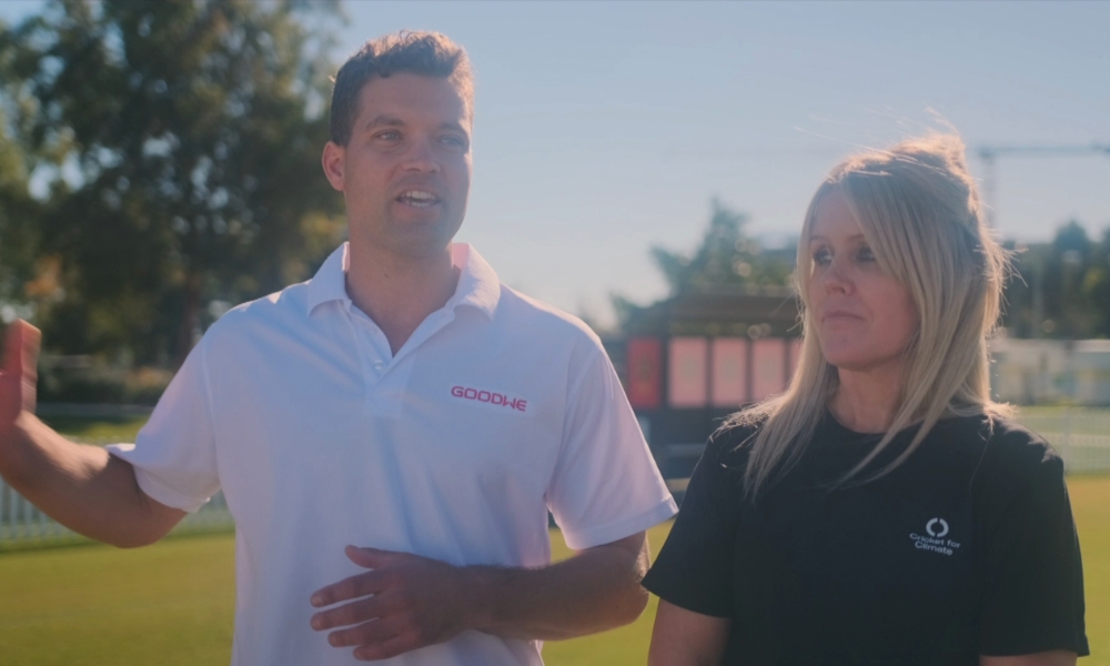 Man in a white polo with a GOODWE logo speaks while a woman in a dark shirt listens outdoors on a sunny day on a field. Man in a white polo with a GOODWE logo speaks while a woman in a dark shirt listens outdoors on a sunny day on a field.