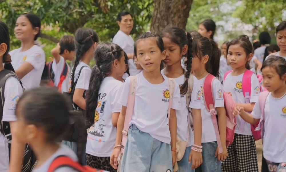 Group of elementary students in white shirts with backpacks outdoors; center girl faces the camera during a school outing. Group of elementary students in white shirts with backpacks outdoors; center girl faces the camera during a school outing.
