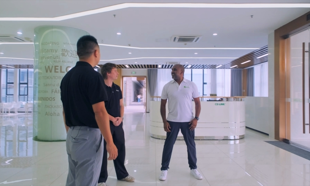 Three men stand and chat in a bright, modern lobby with a curved reception desk in the background. Three men stand and chat in a bright, modern lobby with a curved reception desk in the background.