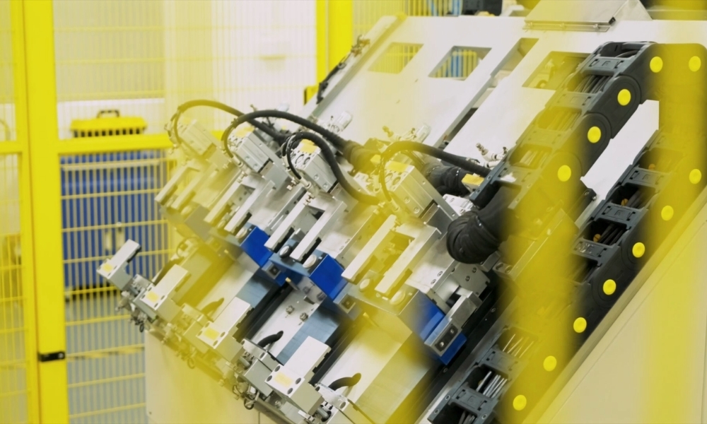 Close-up of automated manufacturing equipment with metal fixtures inside a yellow safety enclosure in a factory setting. Close-up of automated manufacturing equipment with metal fixtures inside a yellow safety enclosure in a factory setting.
