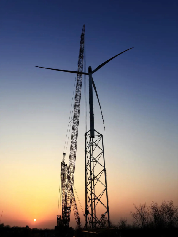 Wind turbine being installed near sunset with a crane towering beside it Wind turbine being installed near sunset with a crane towering beside it