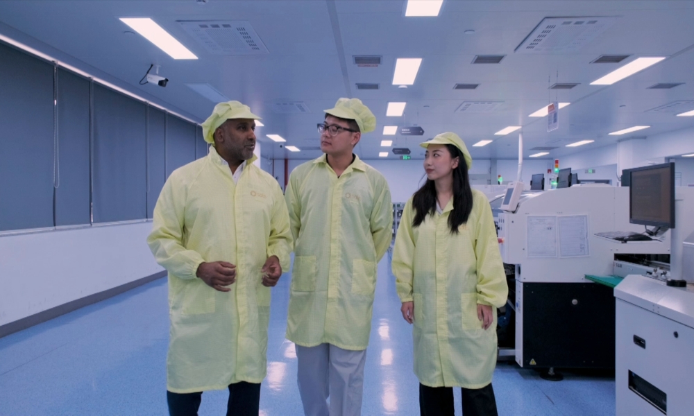 Three people in yellow cleanroom gowns and caps stand together in a high-tech laboratory hallway. Three people in yellow cleanroom gowns and caps stand together in a high-tech laboratory hallway.
